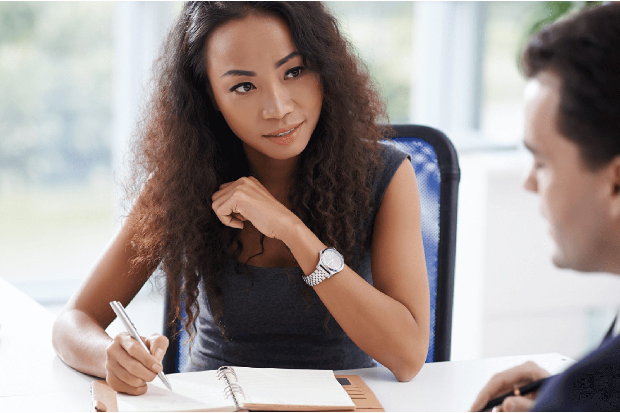 Female professional taking notes during a business meeting, actively listening to a colleague.